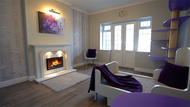Lilac colour-themed cat suite showing most of the room, including fireplace, doors and windows, large bed and play wall.